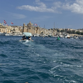 Boat crossing Malta’s Grand Harbour with historic waterfront buildings behind it